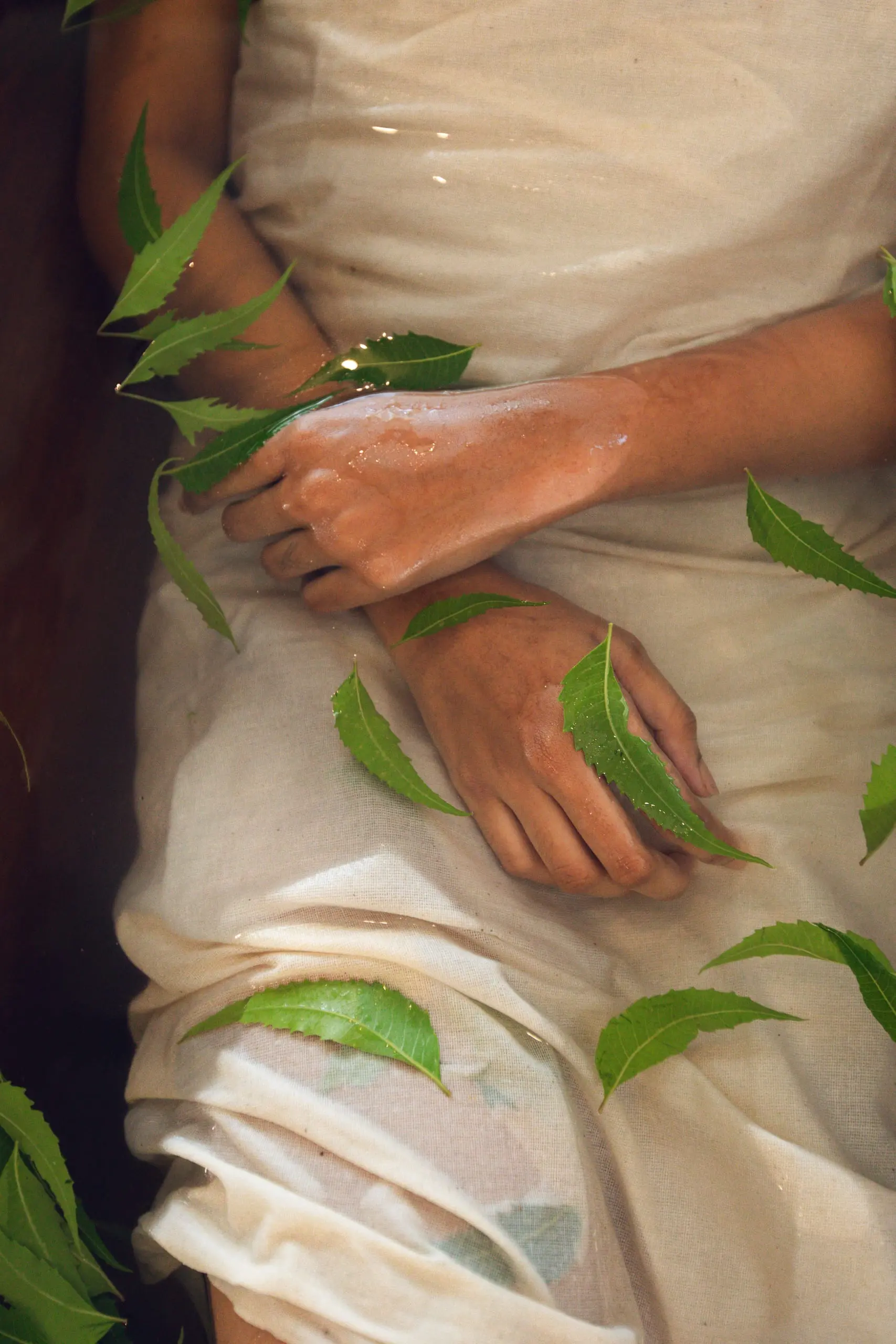 Hands at rest in a leaf-strewn bath, water bright on the skin.
