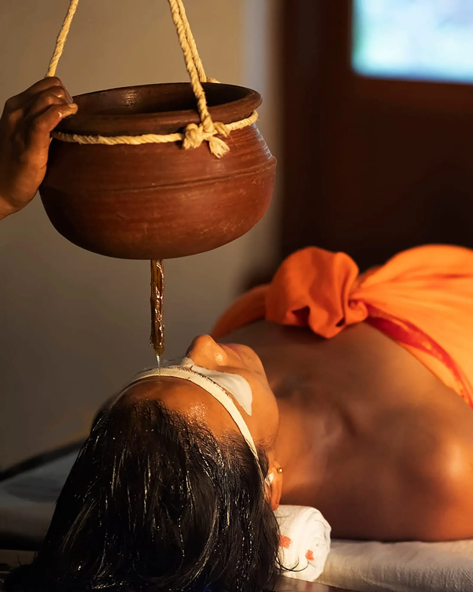 Warm oil falls from a hanging clay pot to the guest's forehead.