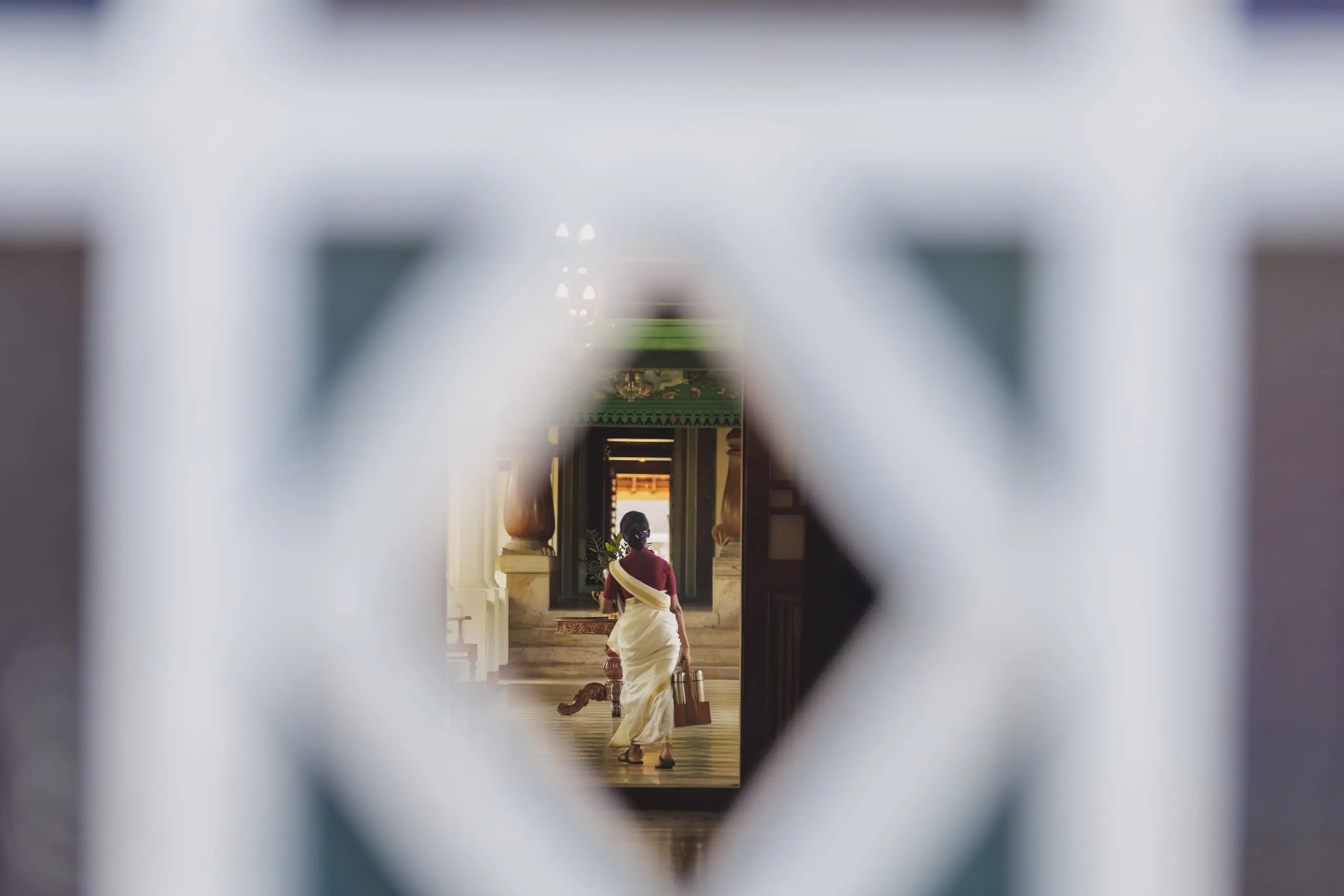 Seen through a white lattice, a practitioner walks a pillared corridor, linens in hand.