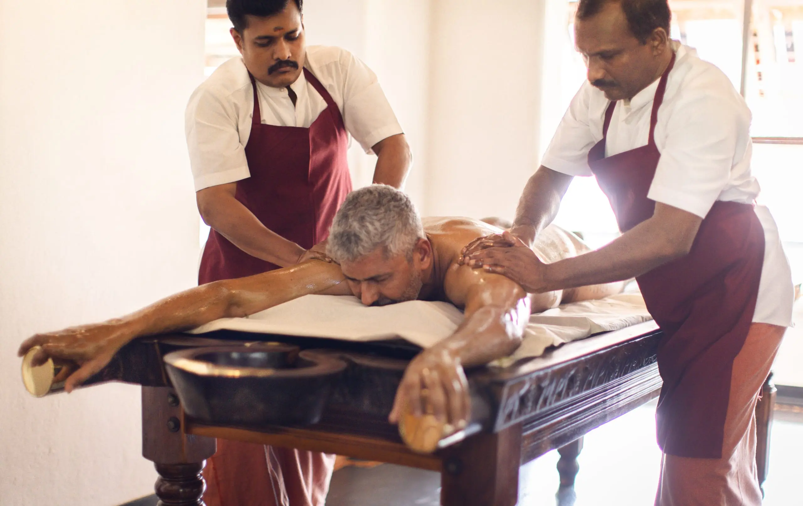 Warm oil worked along a guest's body in synchronised strokes, on a carved wooden table.