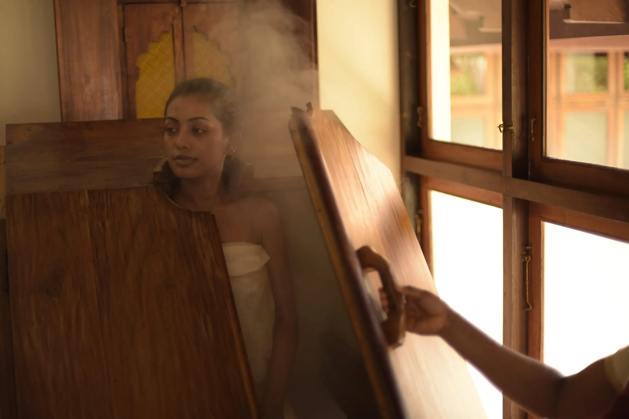 A guest seated in a wooden steam chest, head free, as the herbal steam rises.