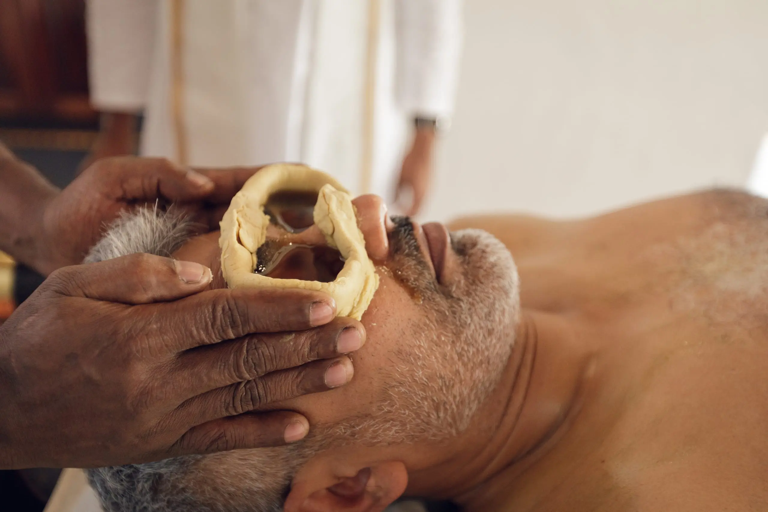 Rings of dough hold warm oil over a guest's closed eyes.